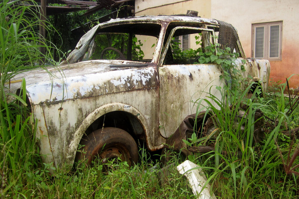 Abandoned car in tall grass outside of a home.