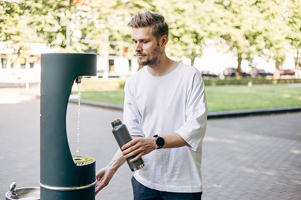 Man refilling his water bottle at the city. Free public water bottle fill station